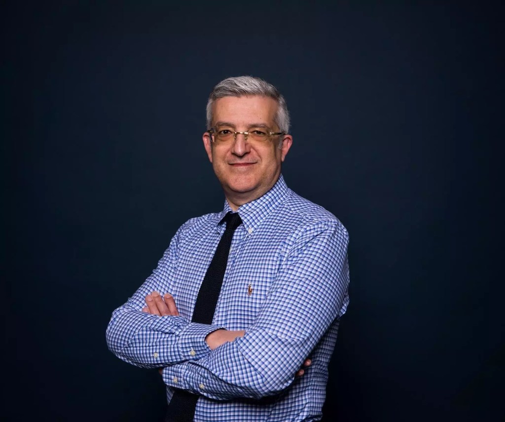 a man with a blue shirt standing in front of a dark background